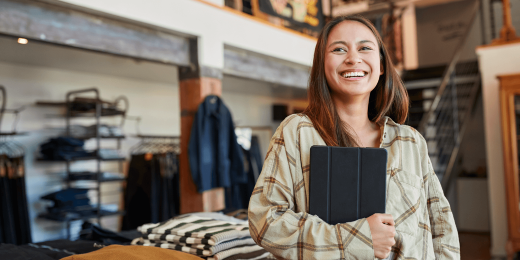business owner smiling inside store holding a tablet after saving money on business insurance