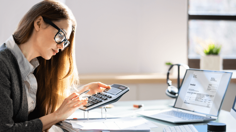 Female accountant working at a desk with a calculator and laptop displaying an invoice