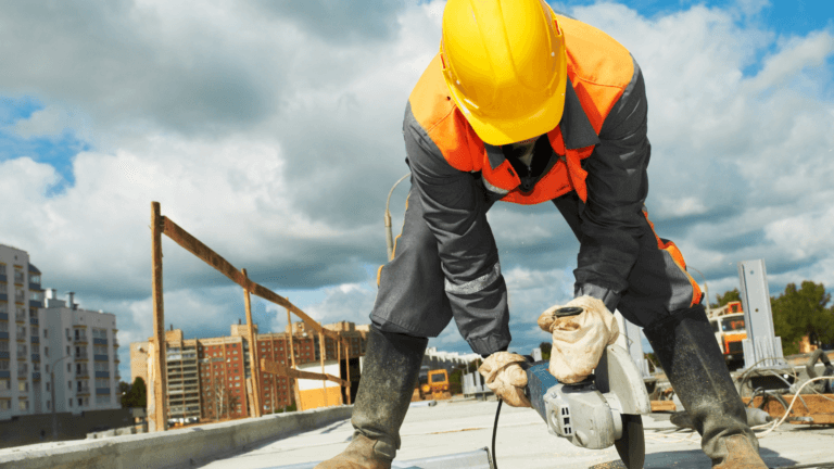 Construction worker wearing safety gear using a power tool on a building site