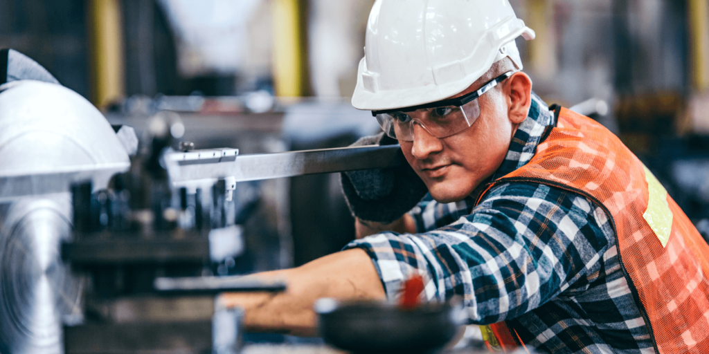Factory worker in safety gear operating machinery and taking measurements.
